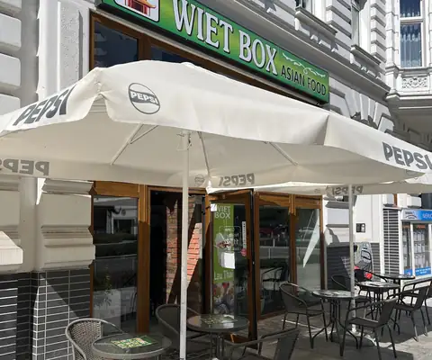Wejście do Wiet Box z zielonym szyldem i ogródkiem pod parasolami